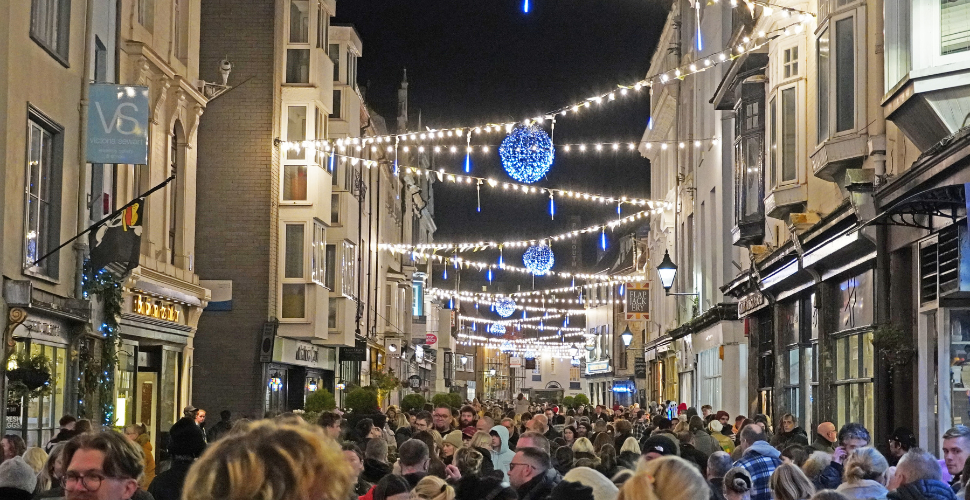 “Crowded city street at night with festive lights and blue ornaments hanging above.